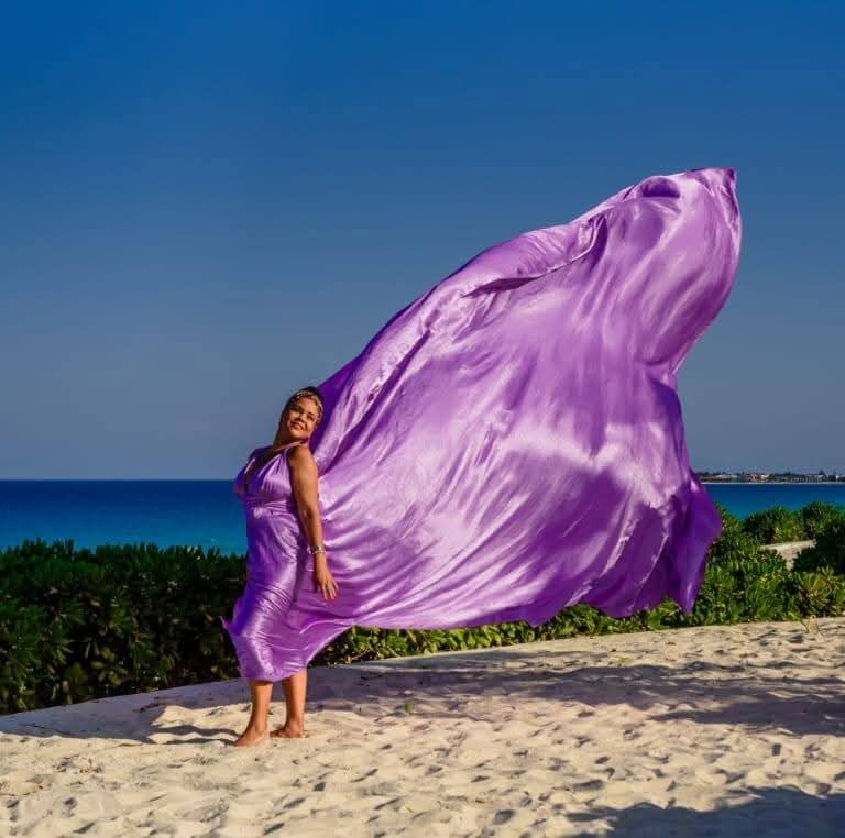 Neuz Ferreira en la playa con una tela violeta ondeando al viento
